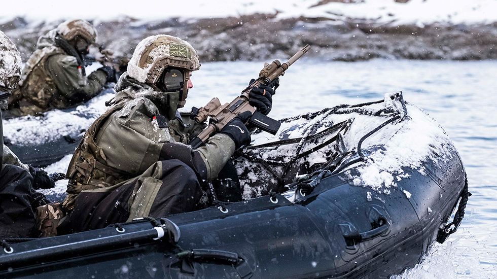 royal marines in fatigues approaching coast in semi rigid boats in snowy, wintry conditions