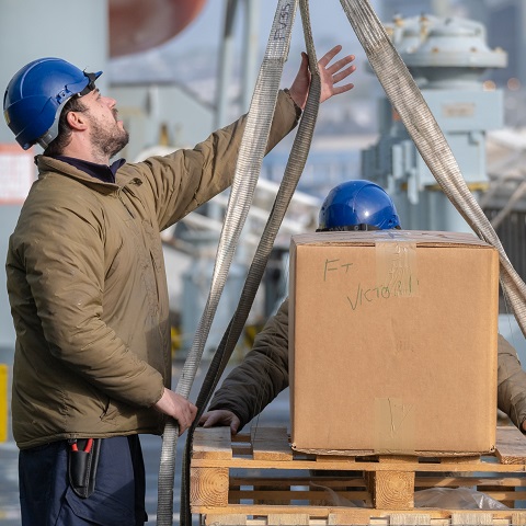 rfa able seaman, dressed light brown jacket and blue safety helmet, guiding a loaded pallet onto deck