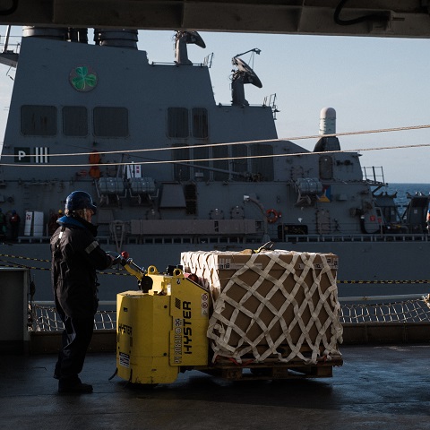 navy blue-dressed rfa able seaman wearing blue safety helmet pushing netted palletised item on pallet truck across deck