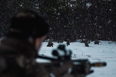 In the foreground a Royal Marine watches a fireteam advance to an enemy position in the snow.