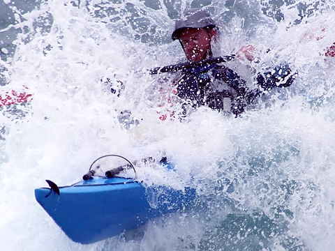 Navy kayaker in royal blue kayak coming through spray from rapids