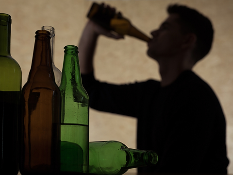 silhouette of person drinking alcohol direct from bottle with empty bottles in foreground