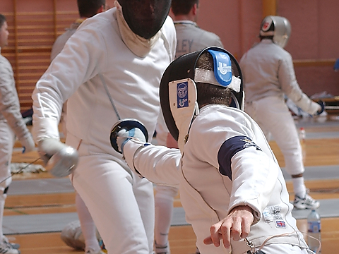 royal navy fencer on advance attack, striking opponent under right armpit at indoor event, with other competitors in background