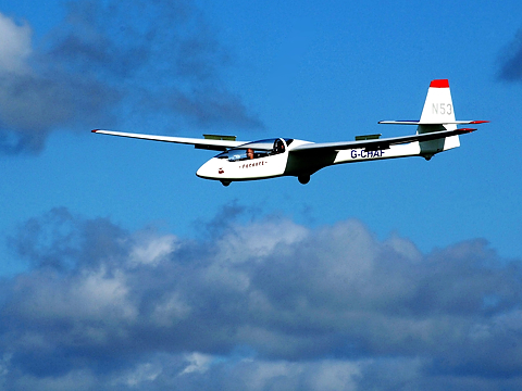 glider coming in to land with blue sky and light grey clouds in background
