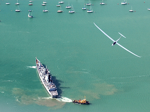 glider banking over frigate entering port
