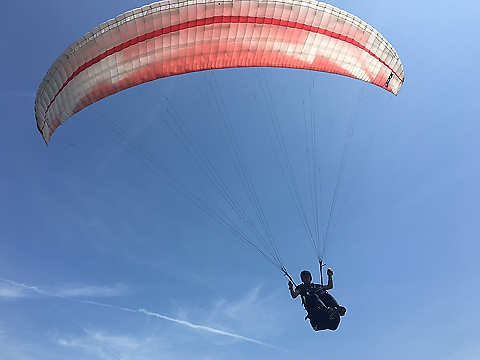 hang glider, mainly in silhouette, under red canopy against a bright blue sky
