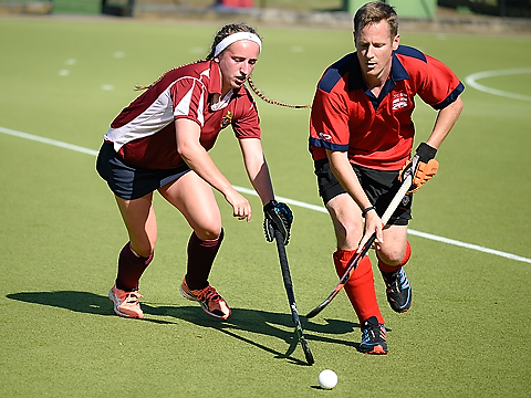 male royal hockey player in red and blue taking on female opponent in red and white kit