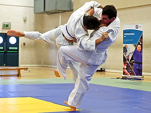 two judokas, one throwing the other clear of the floor, competing on blue and yellow mat