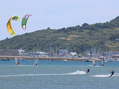 two kite surfers riding the waves off the british coast on a clear day, with windsurfers in background