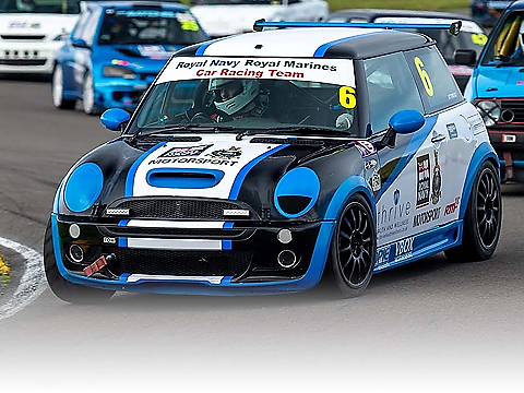 royal navy mini racing car, logoed and liveried in dark blue, white and light blue, taking a right hand turn at speed