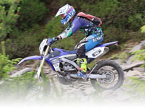 motocross or enduro racer accelerating on rocky trail through wooded area