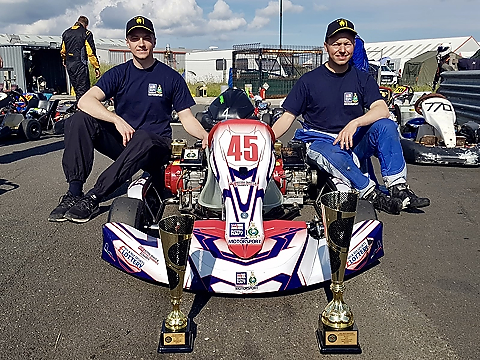 royal navy kart drivers sitting either side of blue and white RN liveried number 45 kart with trophies on display at front