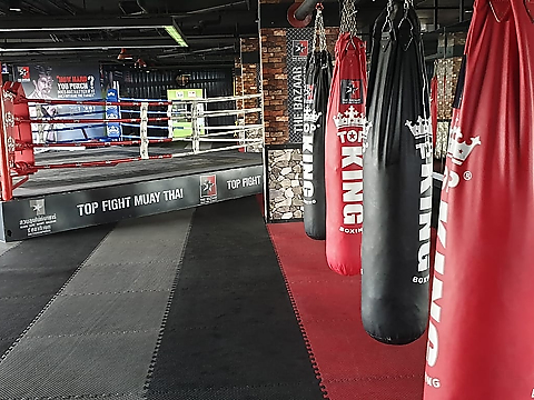 series of red and black punch bags in muay thai gym with a fighting ring in the centre background