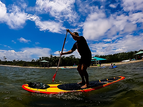 stand up paddle boarder beneath bright blue sky with dappled clouds