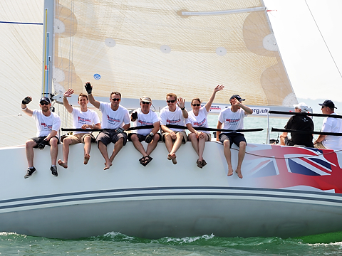 smiling and waving shot of royal navy sailors sat on side of yacht in the ocean