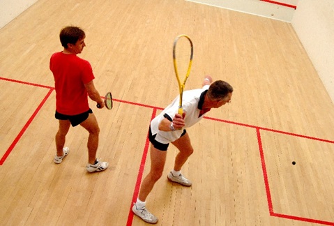 two navy squash players, player on left in red shirt with receiver and shot maker in white shirt
