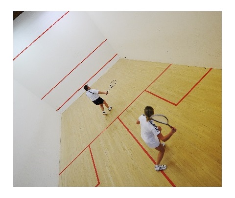 rn squash player in blue and white kit playing backhand shot against wall of court