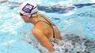 female swimmer in white royal navy cap breaching surface to take breath as she completes breaststroke