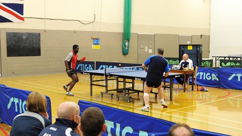 navy player in blue rallying at table tennis table with army counterpart in red