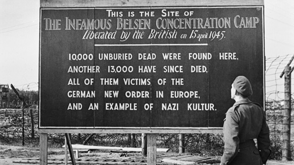 A soldier looks at the sign erected by the liberators of Bergen Belsen about the crimes within