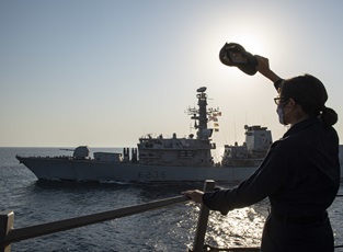 A sailor on USS Sterett waves at HMS Montrose as the US destroyer relieves the British frigate on Operation Sentinel duties