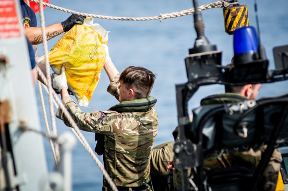 A Royal Marine hands a sailor on HMS Montrose a sack of hashish