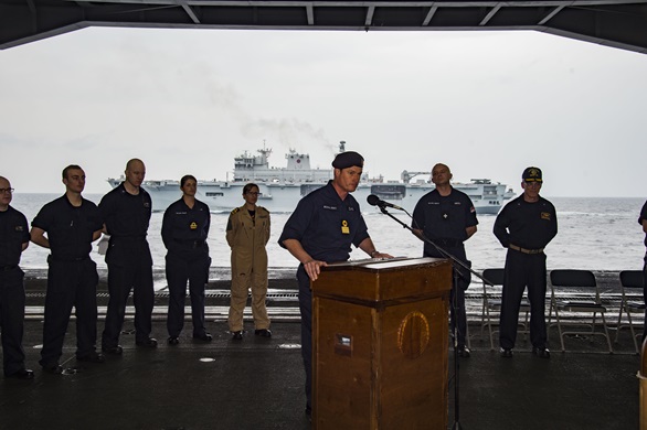 Commodore Andrew Burns speaks during the handover ceremony on board USS Dwight D Eisenhower, with HMS Ocean in the background. Picture: US Navy