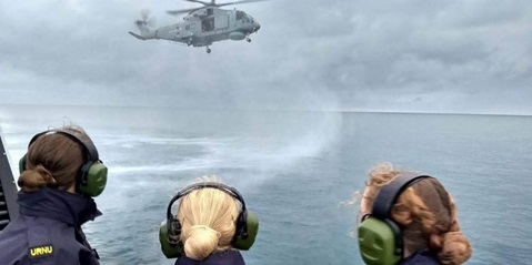 Personnel watching a helicopter over the sea